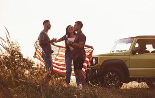 Having conversation. Friends have nice weekend outdoors near theirs green car with USA flag photo