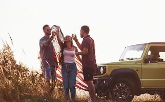 Having conversation. Friends have nice weekend outdoors near theirs green car with USA flag photo