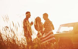 Summertime happiness. Friends have nice weekend outdoors near theirs green car with USA flag photo