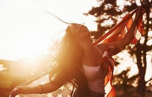 luz hermosa. morena con bandera de estados unidos en las manos diviértete y siente libertad al aire libre en un día soleado foto