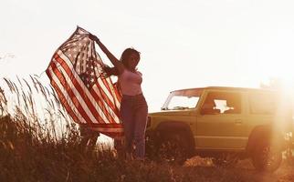 Girl runs forward. Friends have nice weekend outdoors near theirs green car with USA flag photo