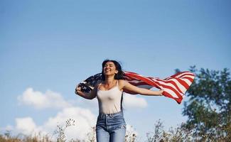 patriota femenina corre con la bandera de estados unidos en las manos al aire libre en el campo contra el cielo azul foto