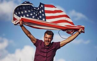 Patriotic happy man waving American Flag against cloudy blue sky photo