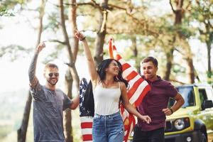 In the forest. Friends have nice weekend outdoors near theirs green car with USA flag photo