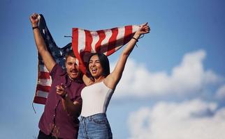 With hands up. Feels freedom. Beautiful couple with American Flag have a good time outdoors in the field photo