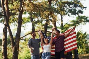 In the forest. Friends have nice weekend outdoors near theirs green car with USA flag photo