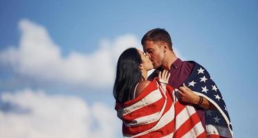 Kissing each other. Feels freedom. Beautiful couple with American Flag have a good time outdoors in the field photo