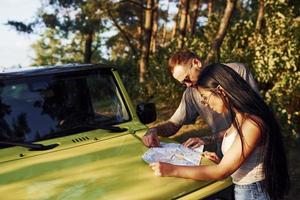 jóvenes amigos leyendo el mapa que está en el capó del moderno jeep verde en el bosque foto