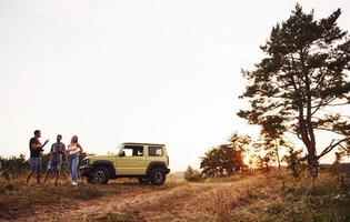 Rural scene. Group of cheerful friends have nice weekend at sunny day near theirs green car outdoors photo