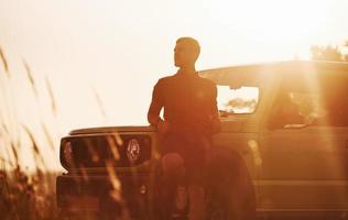 Portrait of man that leaning on green car at beautiful sunny day outdoors in the field photo