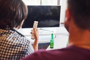 Rear view of friends watching TV and holds remote controller in hand photo