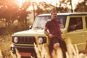 retrato de un hombre que se apoya en un auto verde en un hermoso día soleado al aire libre en el campo foto