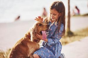 Playful mood. Cute little girl have a walk with her dog outdoors at sunny day photo