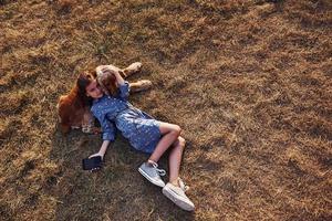 Top view. Lying on the grass with black phone. Cute little girl have a walk with her dog outdoors at sunny day photo