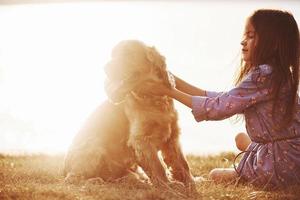 Illuminated by beautiful sunlight. Cute little girl have a walk with her dog outdoors at daytime photo