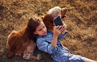 Top view. Lying on the grass with black phone. Cute little girl have a walk with her dog outdoors at sunny day photo