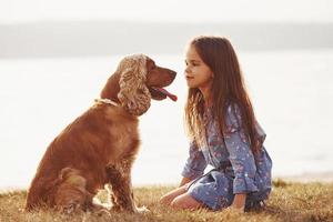 Staring at each other. Cute little girl have a walk with her dog outdoors at sunny day photo