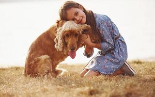 Holding by the hands. Cute little girl have a walk with her dog outdoors at sunny day photo