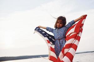 Patriotic female kid with American Flag in hands. Against cloudy sky photo