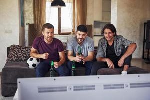 Excited three friends watching soccer on TV at home together photo