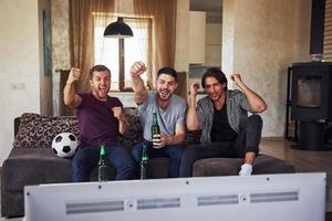 Excited three friends watching soccer on TV at home together photo