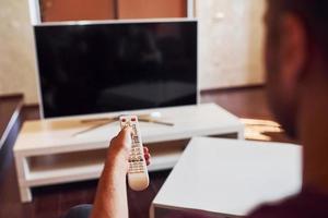 Backing view of man holds remote controller in hand and turning on TV photo