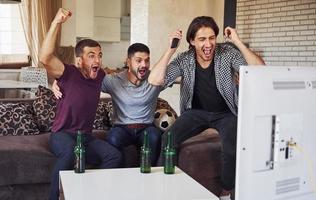 It's a goal. Excited three friends watching soccer on TV at home together photo