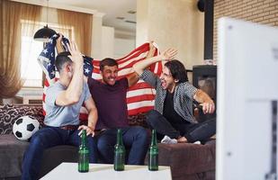 emocionados tres amigos viendo fútbol en la televisión en casa juntos foto