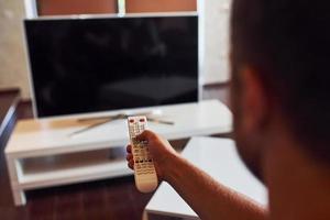 Backing view of man holds remote controller in hand and turning on TV photo