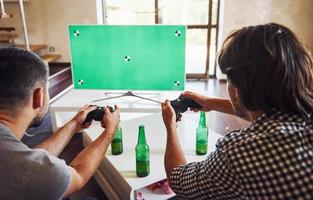 Beer on the table. Group of friends have fun playing console game indoors at living room photo