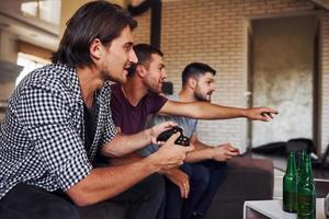 Side view. Group of friends have fun playing console game indoors at living room photo