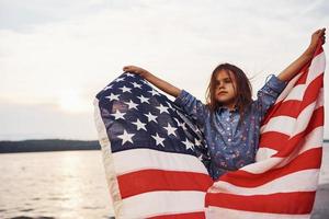 Patriotic female kid with American Flag in hands. Against cloudy sky photo