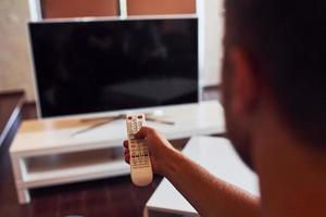 vista trasera del hombre sostiene el control remoto en la mano y enciende la televisión foto