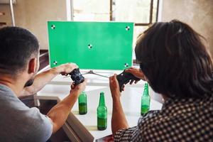 cerveza en la mesa. grupo de amigos se divierten jugando juegos de consola en el interior de la sala de estar foto