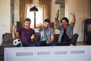 It's a goal. Excited three friends watching soccer on TV at home together photo