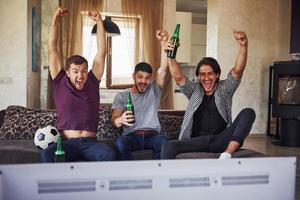 es una meta emocionados tres amigos viendo fútbol en la televisión en casa juntos foto