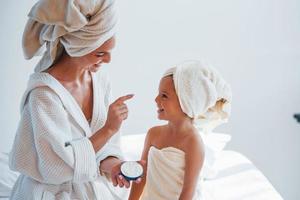 Using cream to clear skin. Young mother with her daugher have beauty day indoors in white room photo