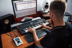 Playing midi keyboard. Sound engineer working and mixing music indoors in the studio photo