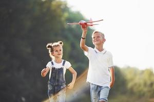 Girl and boy having fun outdoors with red toy airplane in hands photo