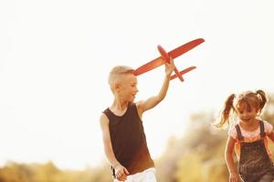 Girl and boy having fun outdoors with red toy airplane in hands photo