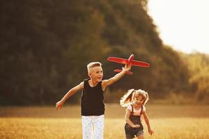 Girl and boy having fun outdoors with red toy airplane in hands photo