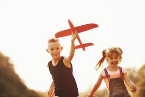 Girl and boy having fun outdoors with red toy airplane in hands photo