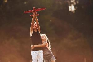 Girl and boy having fun outdoors with red toy airplane in hands photo