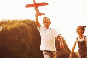 Girl and boy having fun outdoors with red toy airplane in hands photo