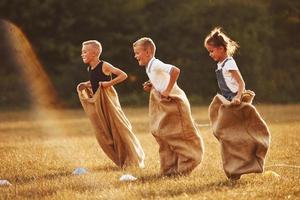 Jumping sack race outdoors in the field. Kids have fun at sunny daytime photo