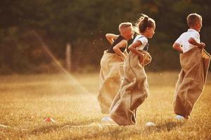 saltando carrera de sacos al aire libre en el campo. los niños se divierten durante el día soleado