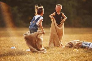 saltando carrera de sacos al aire libre en el campo. los niños se divierten durante el día soleado foto