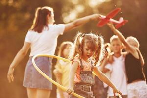 Girl with circle fitness tool. Group of kids have active weekend in the field. Illuminated by beautiful sunlight photo