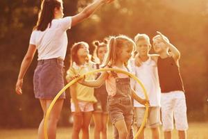 Girl with circle fitness tool. Group of kids have active weekend in the field. Illuminated by beautiful sunlight photo