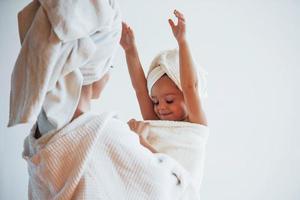 Wearing whiite bathrobes. Young mother with her daugher have beauty day indoors in white room photo